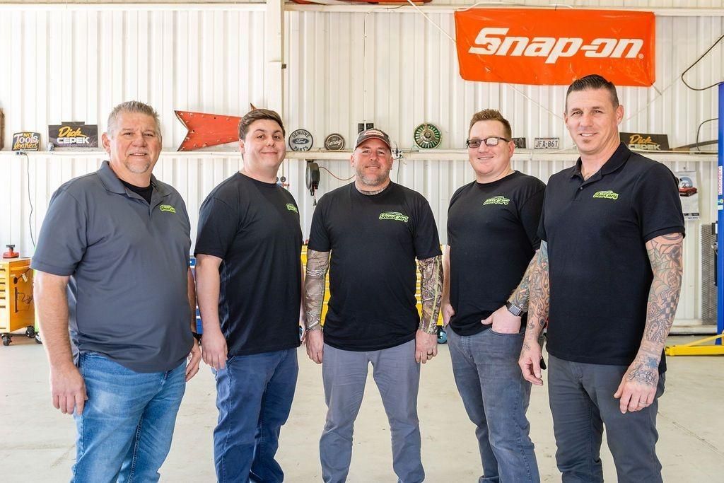 A group of men are posing for a picture in front of a snap on sign.