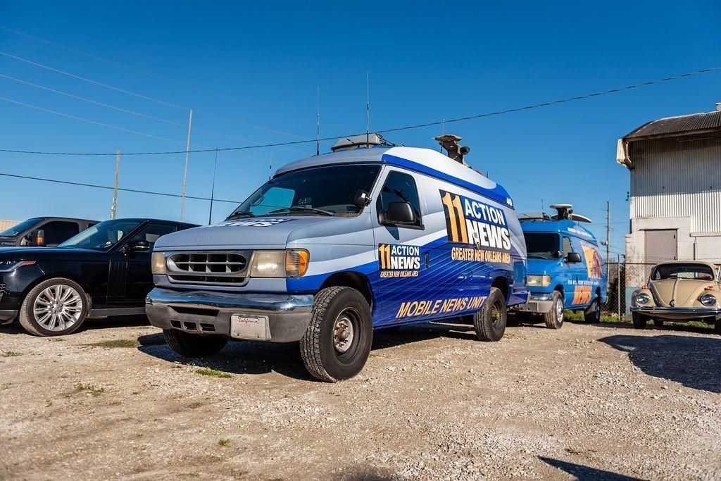 A blue and white van is parked in a gravel lot next to a building.