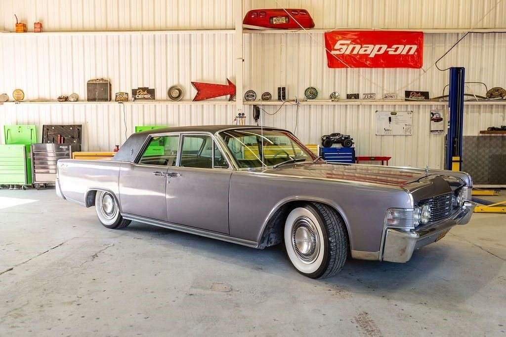 A gray car is parked in a garage next to a snap on sign.