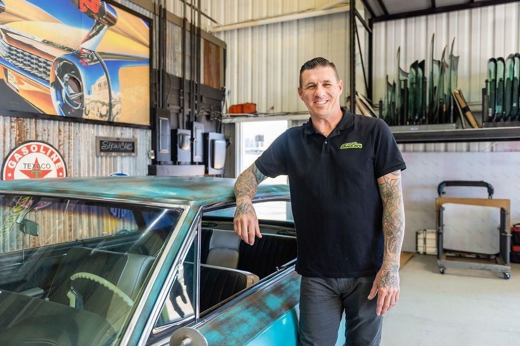A man is standing next to a car in a garage.
