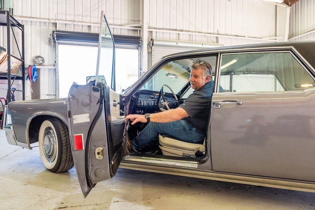 A man is sitting in the driver 's seat of a car with the door open.