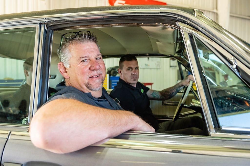 Two men are sitting in a car in a garage.