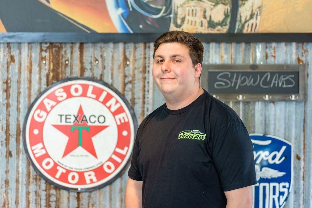 A man is standing in front of a gasoline texaco motor oil sign.