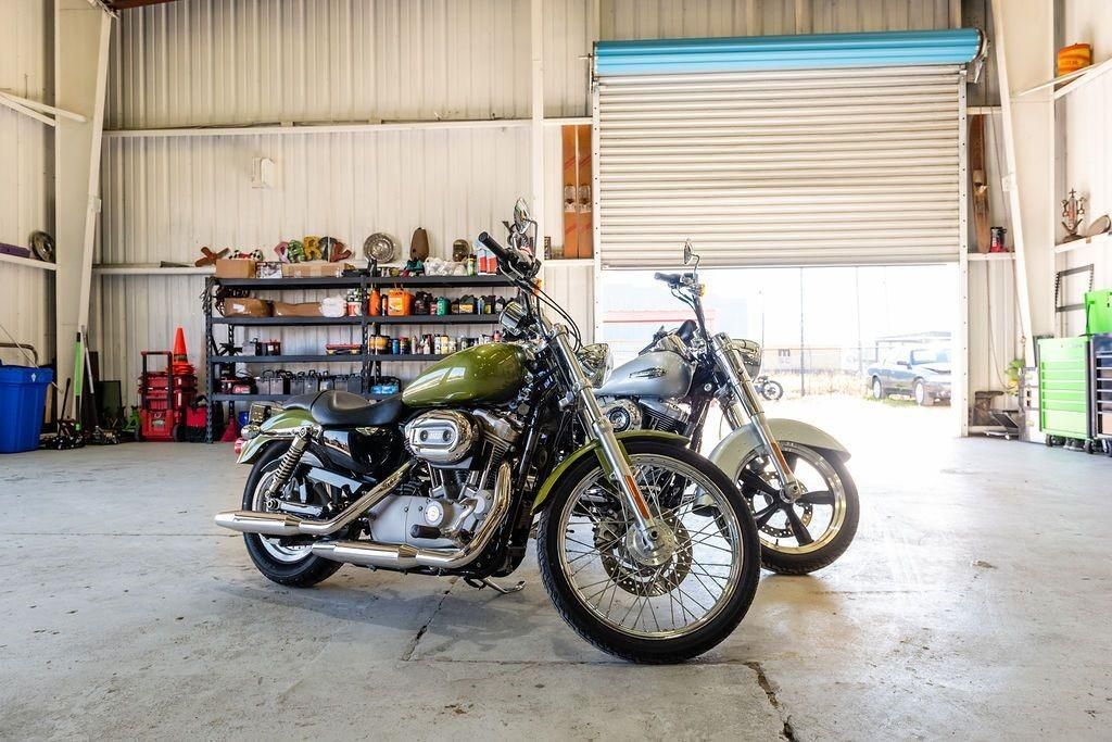 Two motorcycles are parked in a garage with a garage door open.