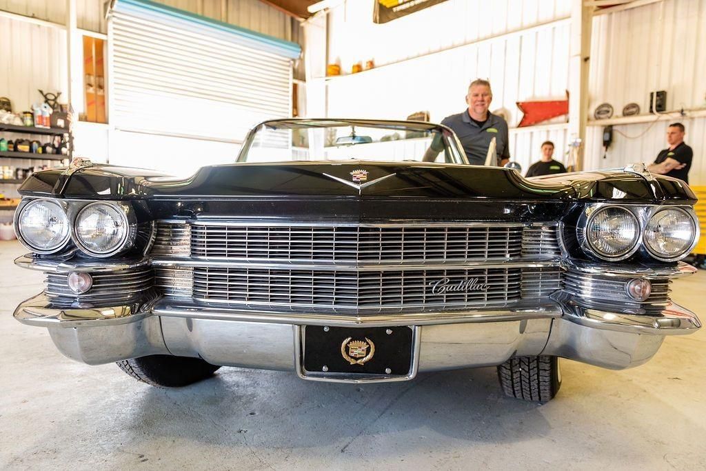 A man is standing next to a black cadillac convertible in a garage.