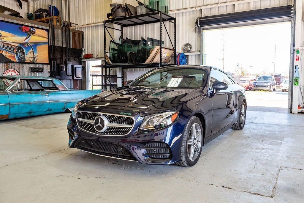 A black mercedes benz e class coupe is parked in a garage.