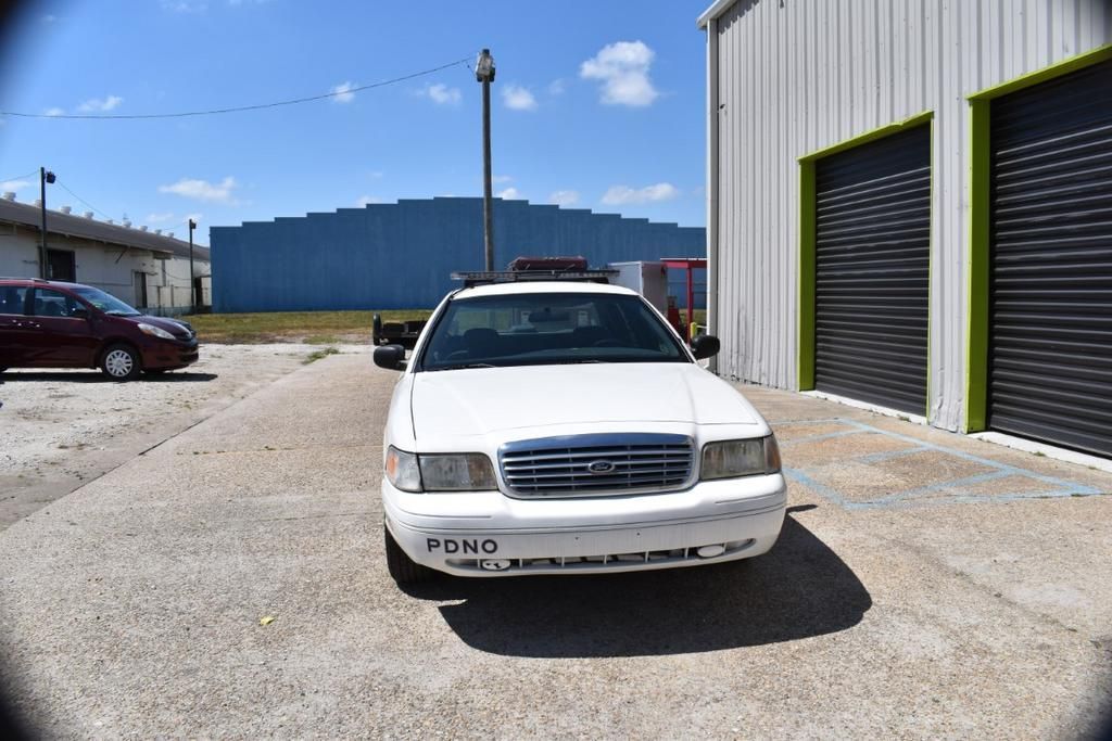 A white ford crown victoria is parked in front of a building.