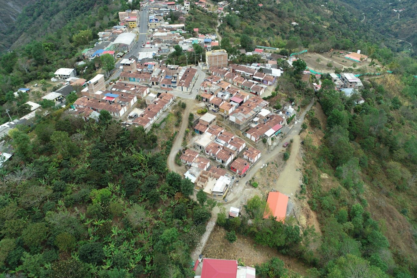 Vista aérea de una ciudad enclavada en un paisaje montañoso y verde con edificios, carreteras y árboles.
