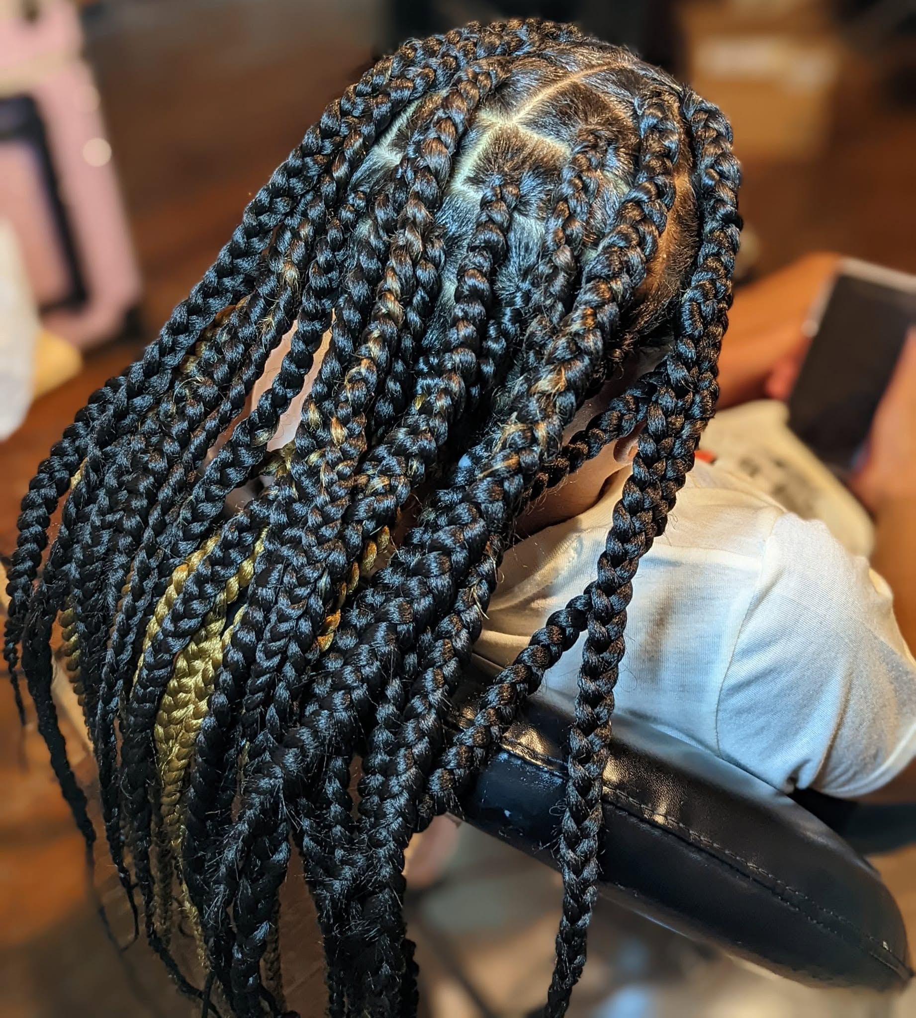 A woman with braids is sitting in a chair looking at her phone.
