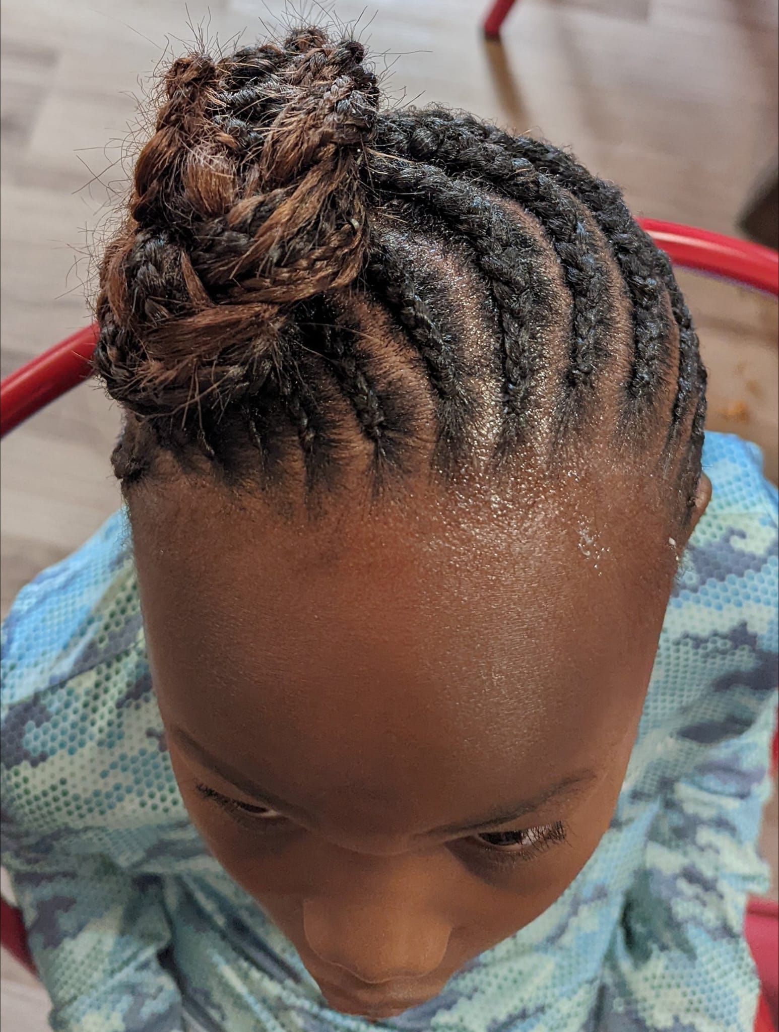 A little girl with braids in a bun is sitting on a chair.