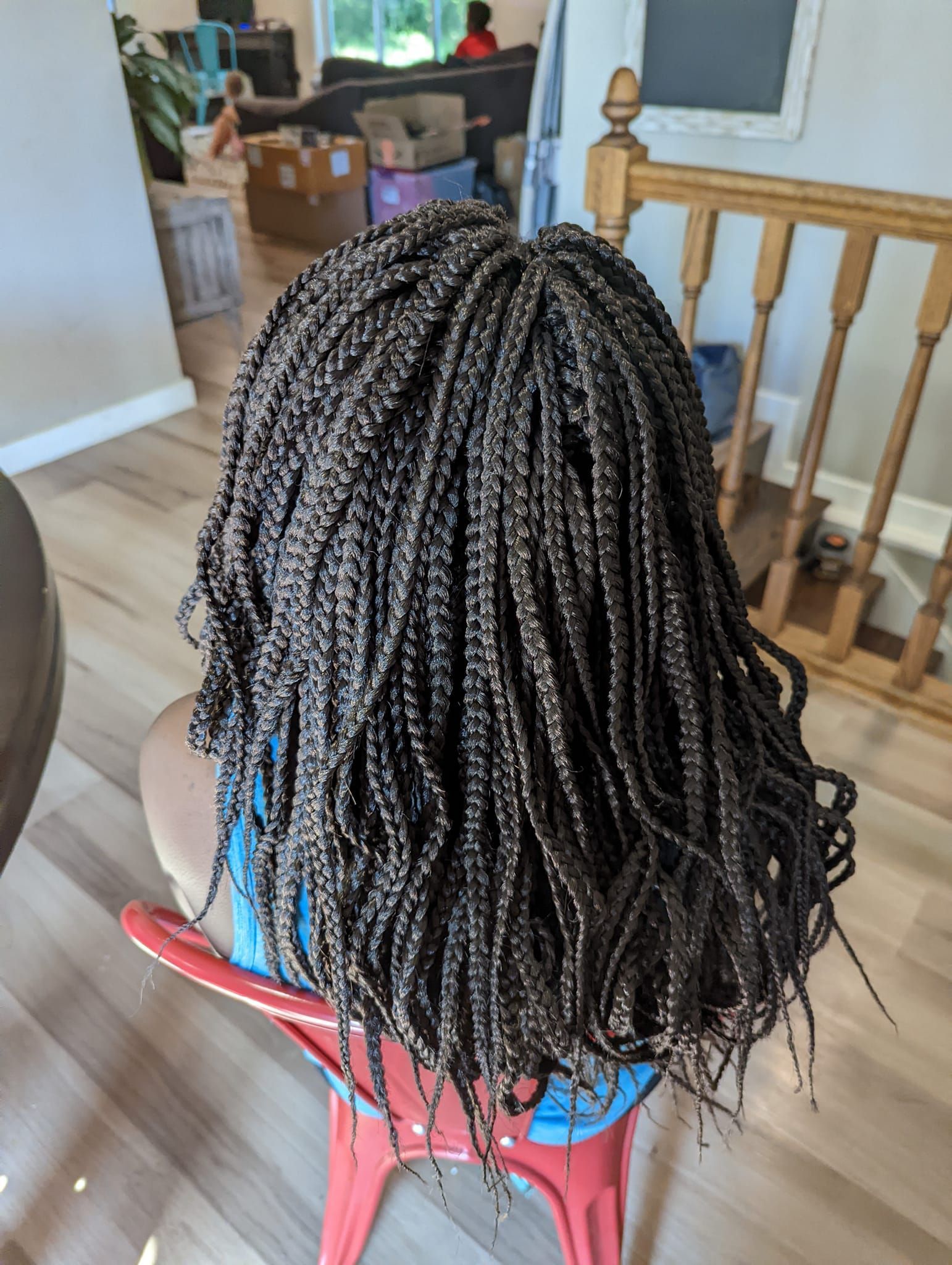 A woman with braids is sitting on a red chair in a living room.