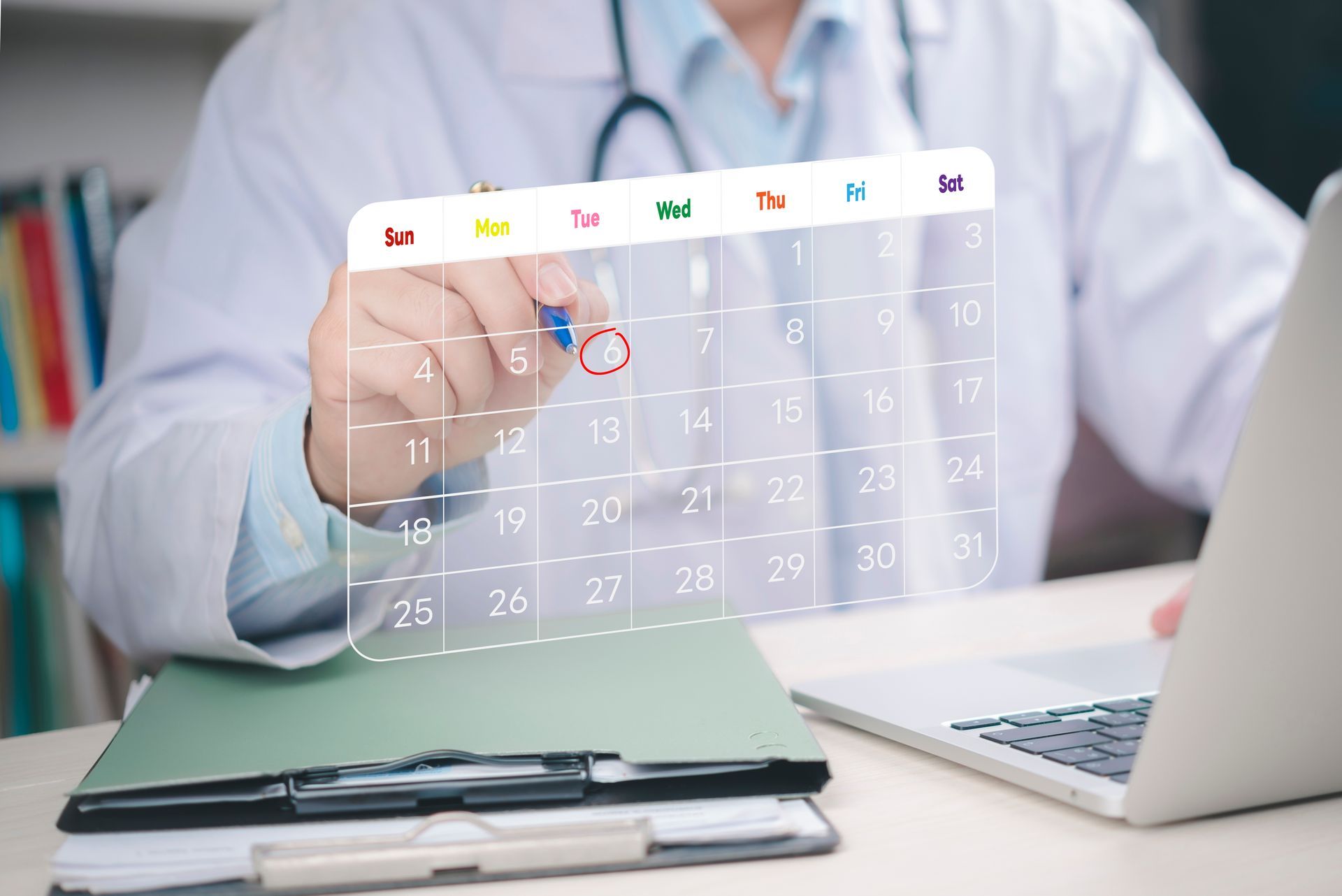 Doctor in lab coat pointing at a calendar on a screen with a pen, next to a laptop and files.