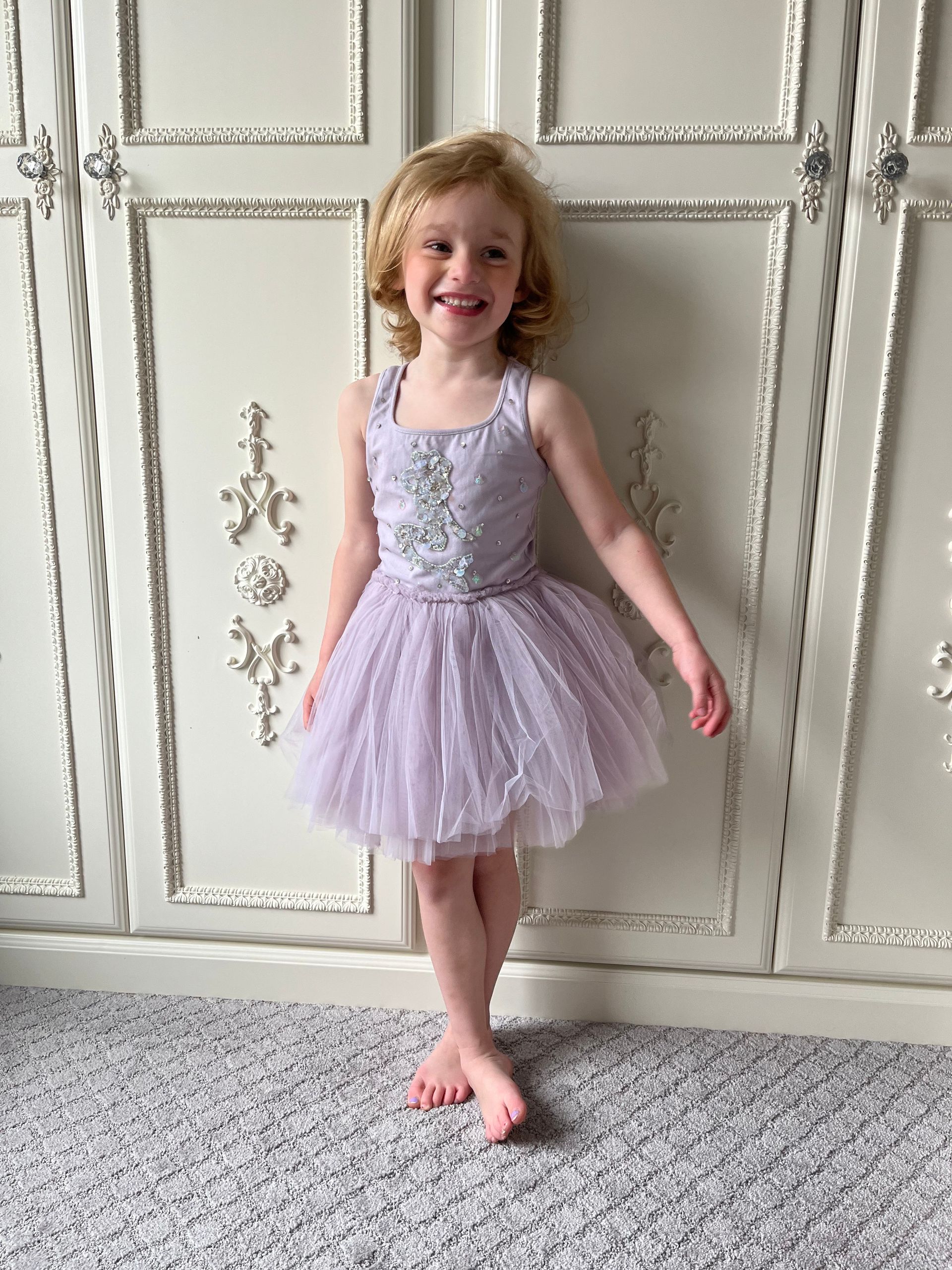 A little girl in a purple dress is standing in front of a white cabinet.