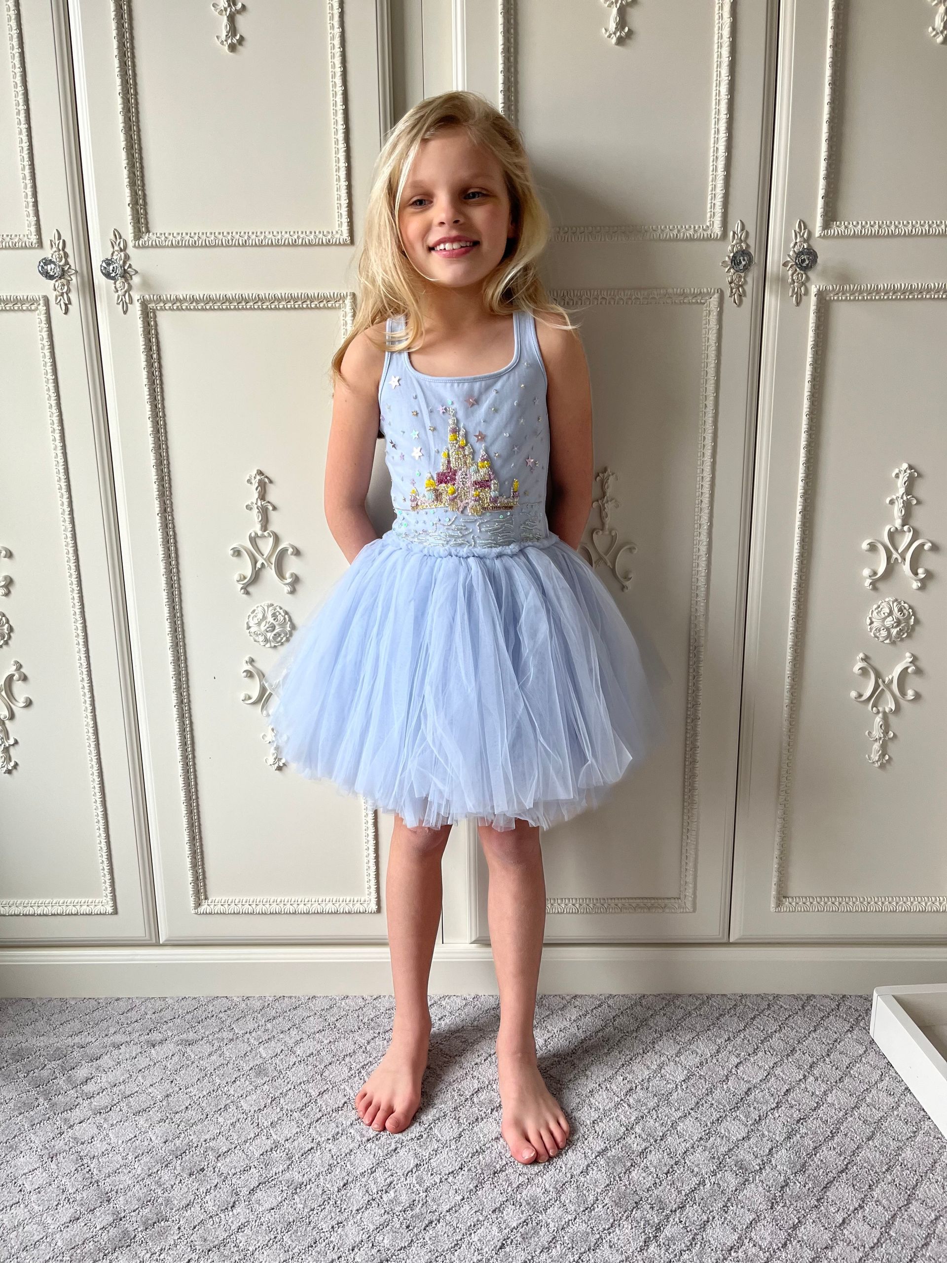 A little girl in a blue dress is standing in front of a closet.