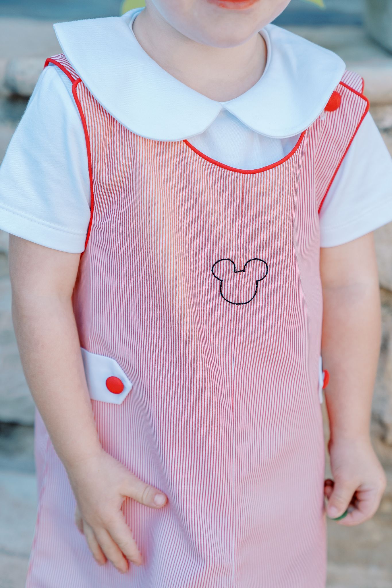 A little girl is wearing a pink overall with a mickey mouse embroidered on it.
