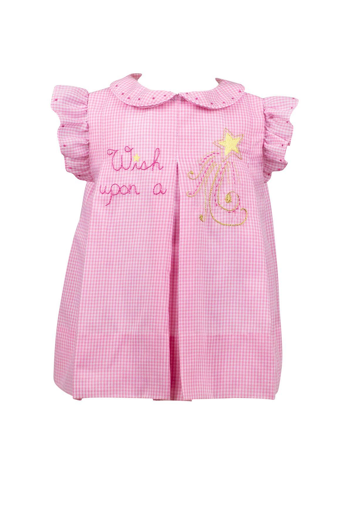 A little girl is wearing a pink dress with a christmas tree on it.