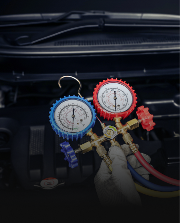 Close-up of gloved hands using gauges to check a car's AC system under the hood.