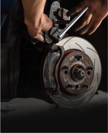 Mechanic working on a car's brake system; hands holding tool near rotor and caliper.