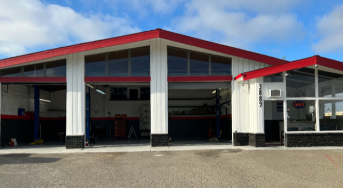 Auto repair shop with red and white exterior, three garage bays, and a small office under a blue sky.