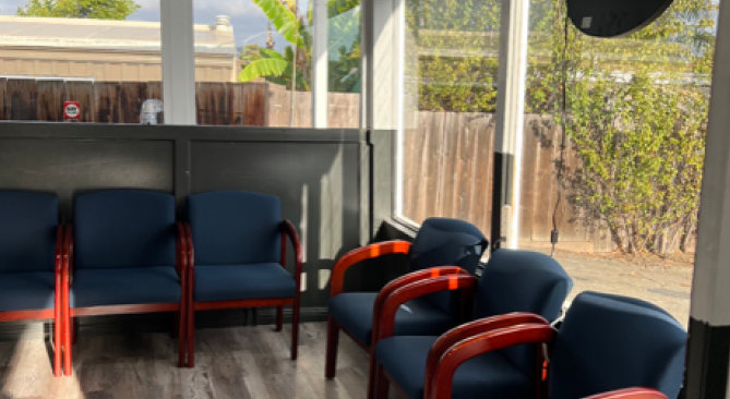 Waiting room with blue chairs, wood trim, and a window overlooking a fence.