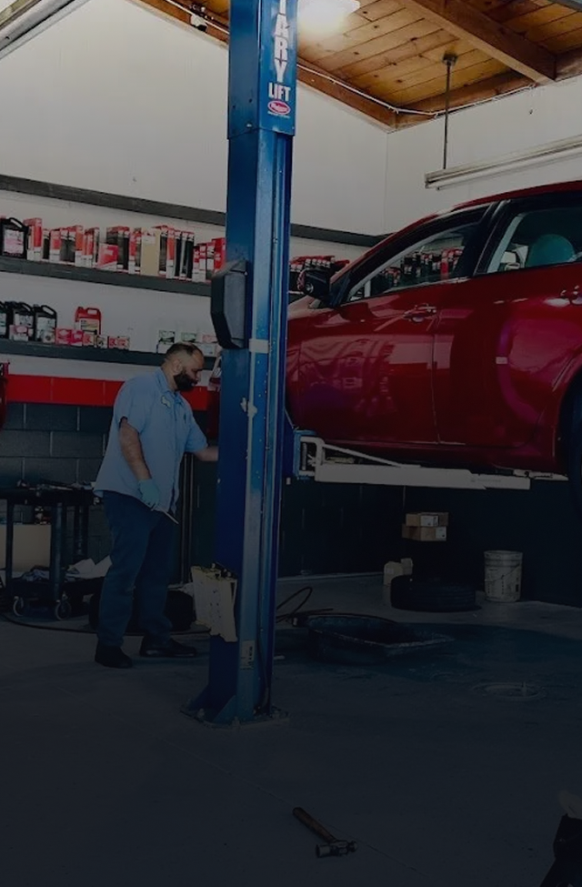 Mechanic inspecting a red car raised on a lift in a garage.