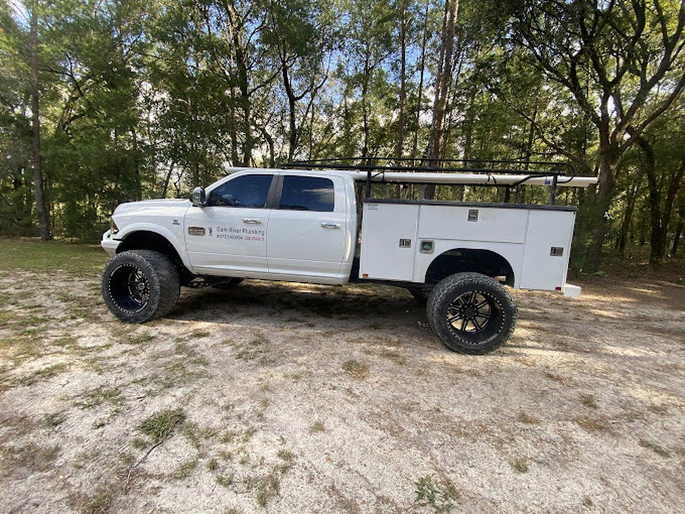 A white truck with a utility bed is parked in a dirt field.