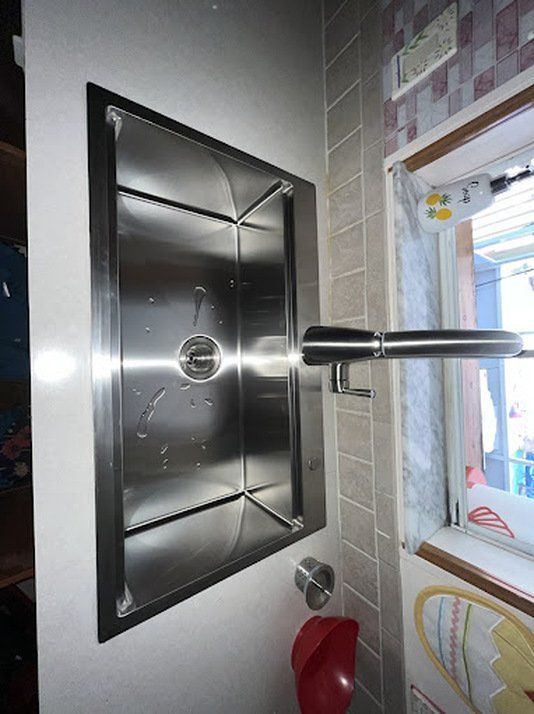 A stainless steel sink in a bathroom next to a window
