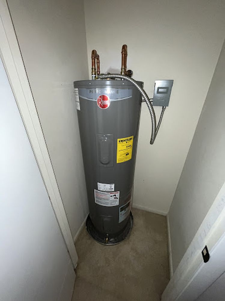 A water heater is sitting in a corner of a room next to a door.