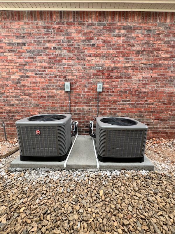 Two air conditioners are sitting on the sidewalk outside of a building.