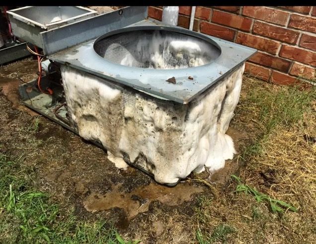 A man is standing on a ladder fixing an air conditioner.