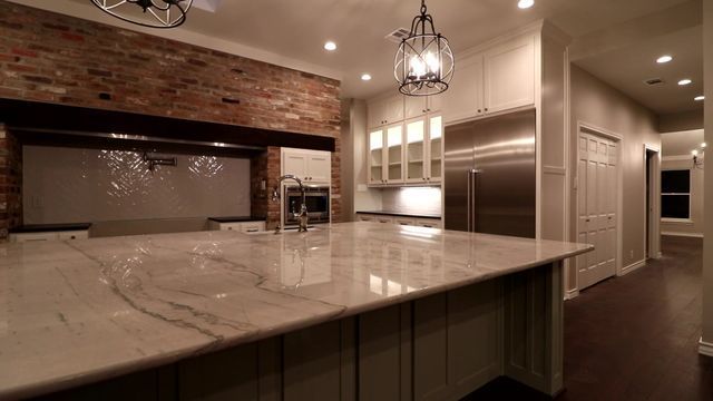 Modern kitchen with large marble island, brick backsplash, pendant lights, and warm ambient lighting.