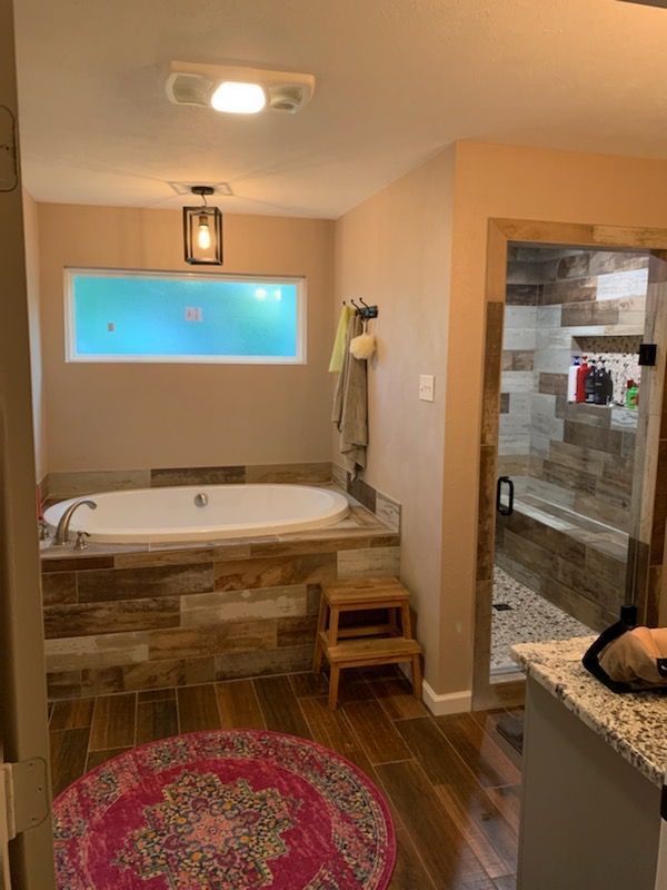 Bathroom with a soaking tub, granite vanity, tiled shower, and a red round rug on wood-look floors