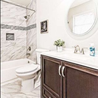 Bright bathroom with marble shower, white toilet, dark wood vanity, round mirror, and small plant decor
