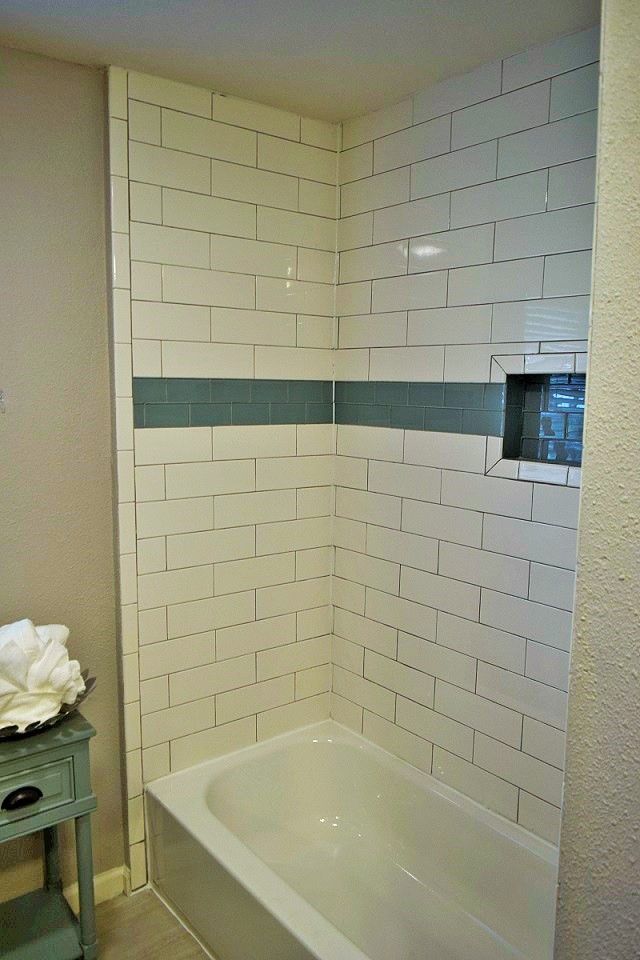 Small bathroom shower with white subway tile, teal accent strip, and a white tub.