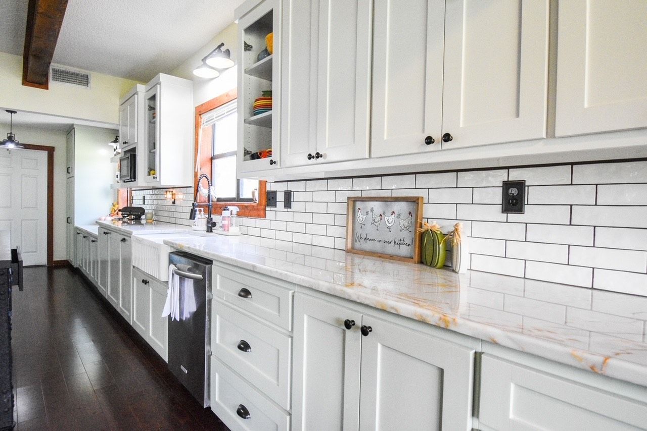 Bright white galley kitchen with subway tile backsplash, marble counters, and dark wood floor