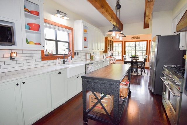 Bright kitchen with white cabinets, black island, hardwood floors, and large windows overlooking a dining area