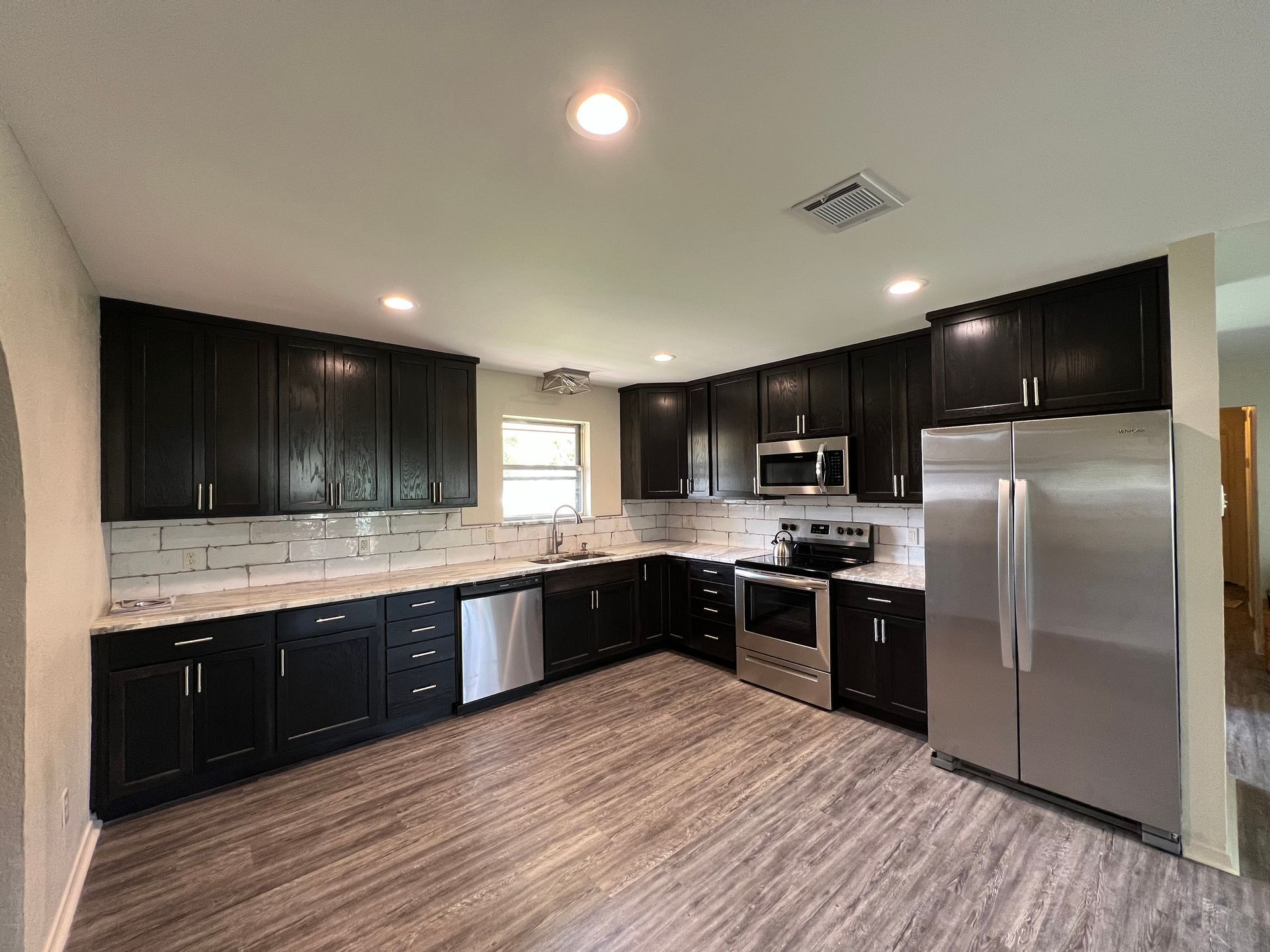 Modern kitchen with dark cabinets, stainless steel appliances, and light tile backsplash