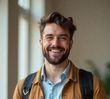 A young man with a beard and a backpack is smiling for the camera.