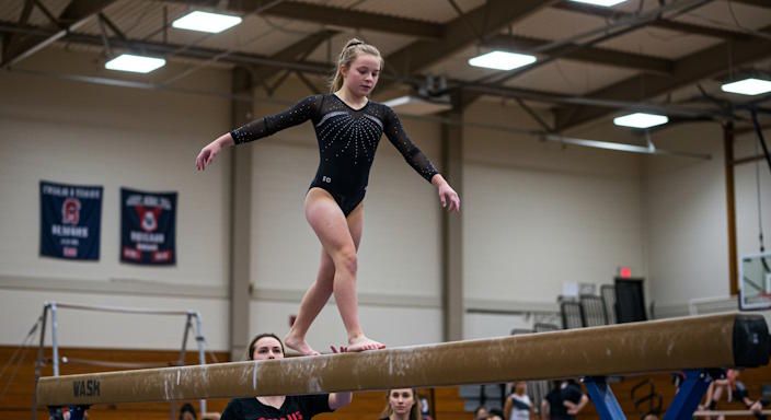 female middle-school gymnast performing on balance beam in Reynoldsburg gym coach offering guidance nearby