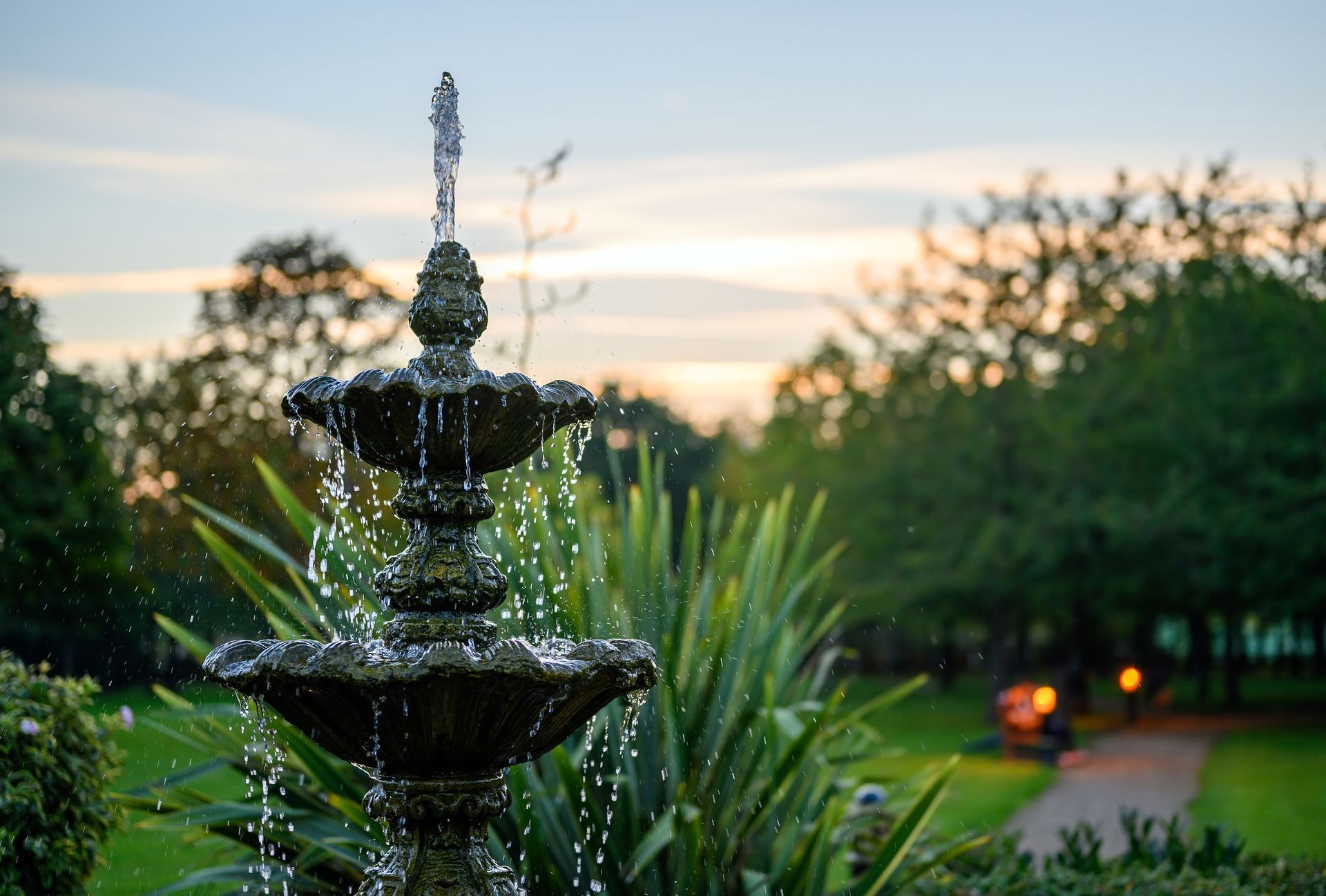 a fountain in a garden with a sunset in the background