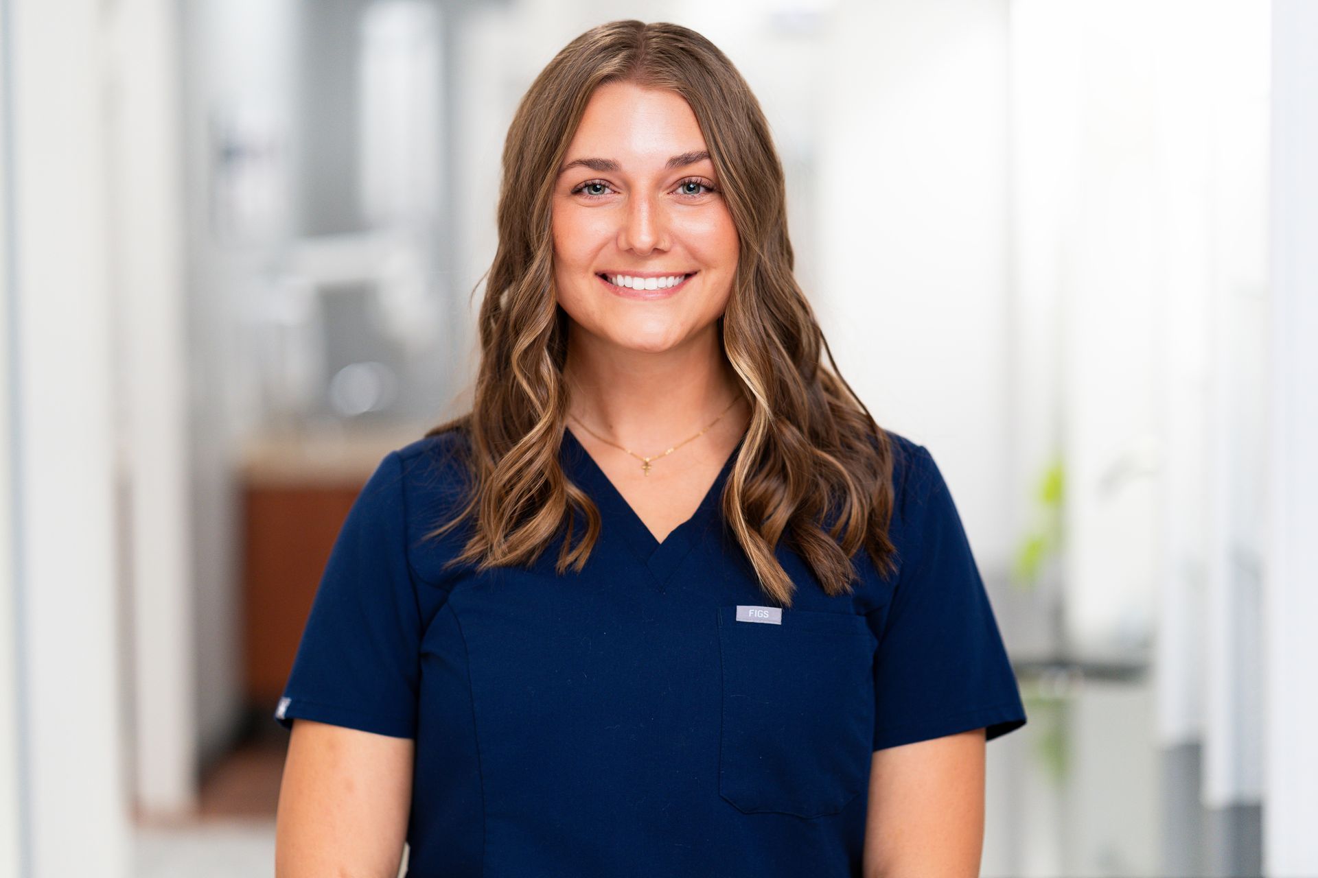 Dentist with arms crossed, smiling, wearing black scrubs, in a dental office.