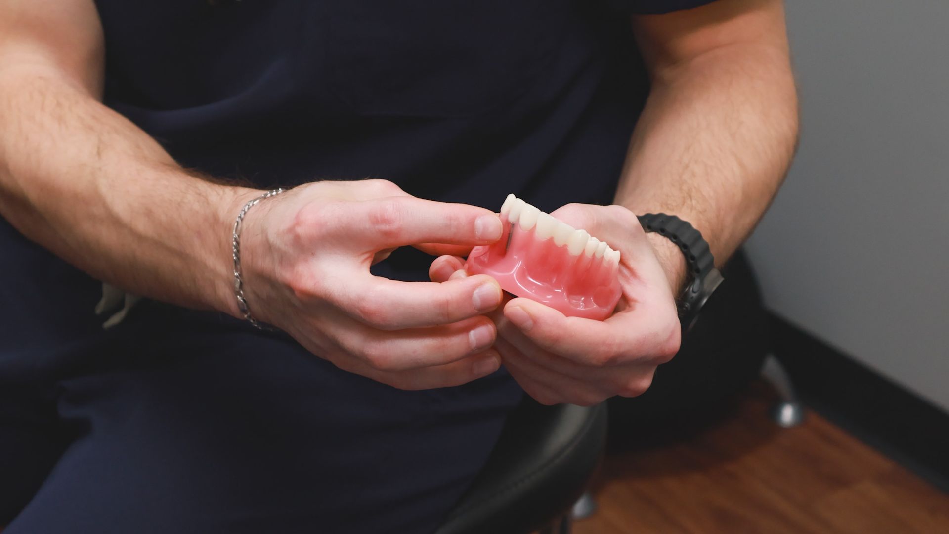 McMahon Dental's technician in blue scrubs inspecting a dental crown in their dental lab.