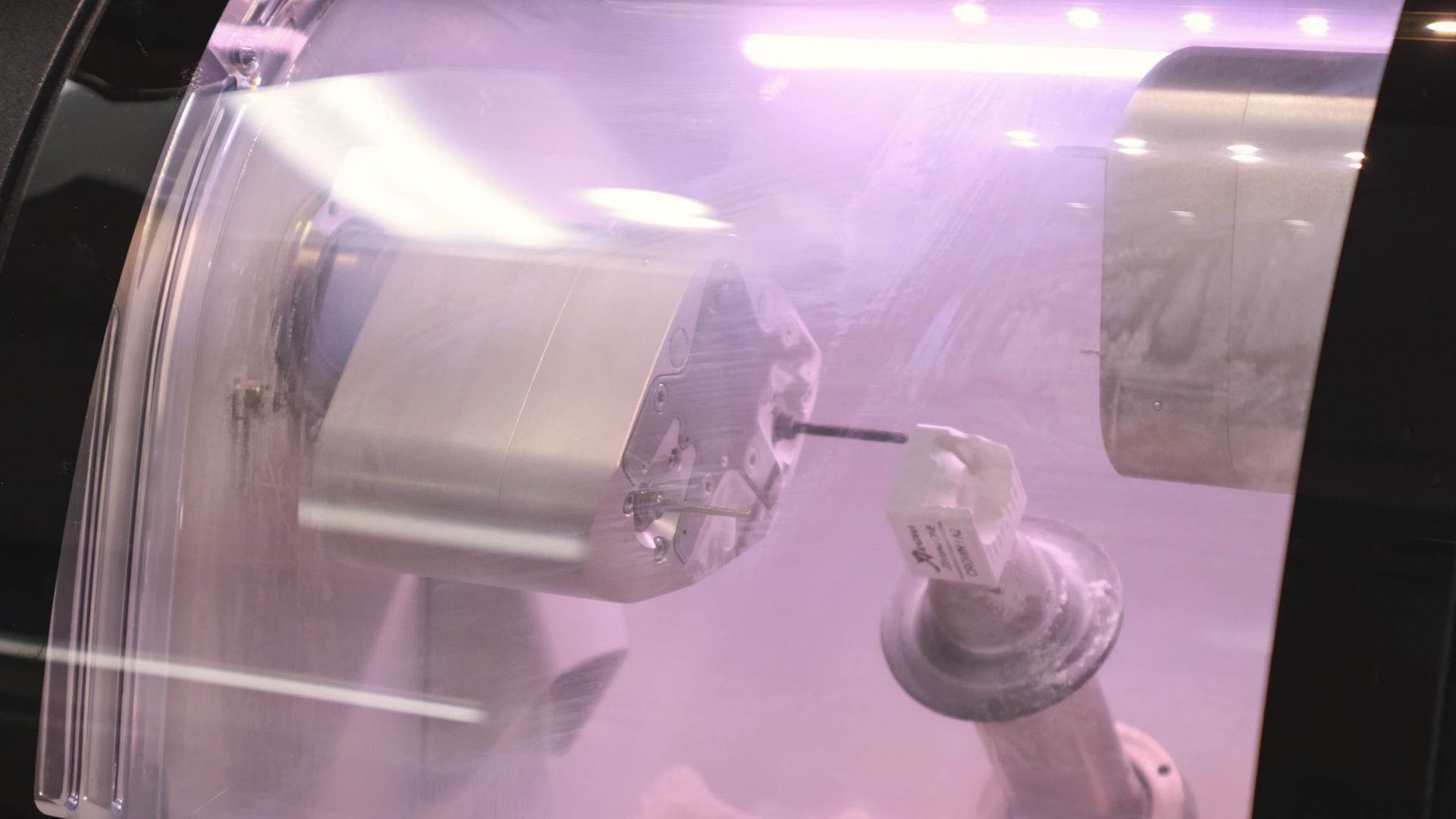 Hand placing a dental crown into a CEREC MC XL milling machine. Gray and white machine with blue light.