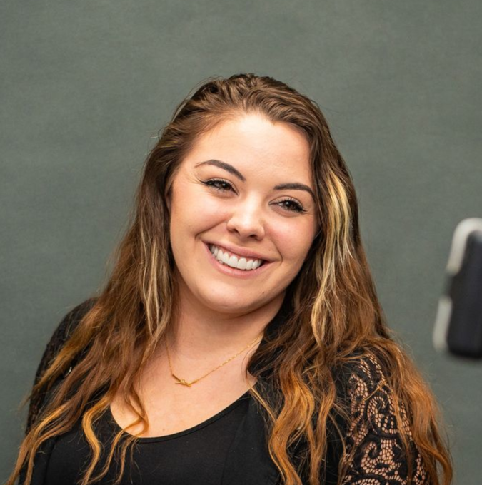 Woman smiling, holding a teeth shade guide showing her results after receiving teeth whitening at McMahon Dental.