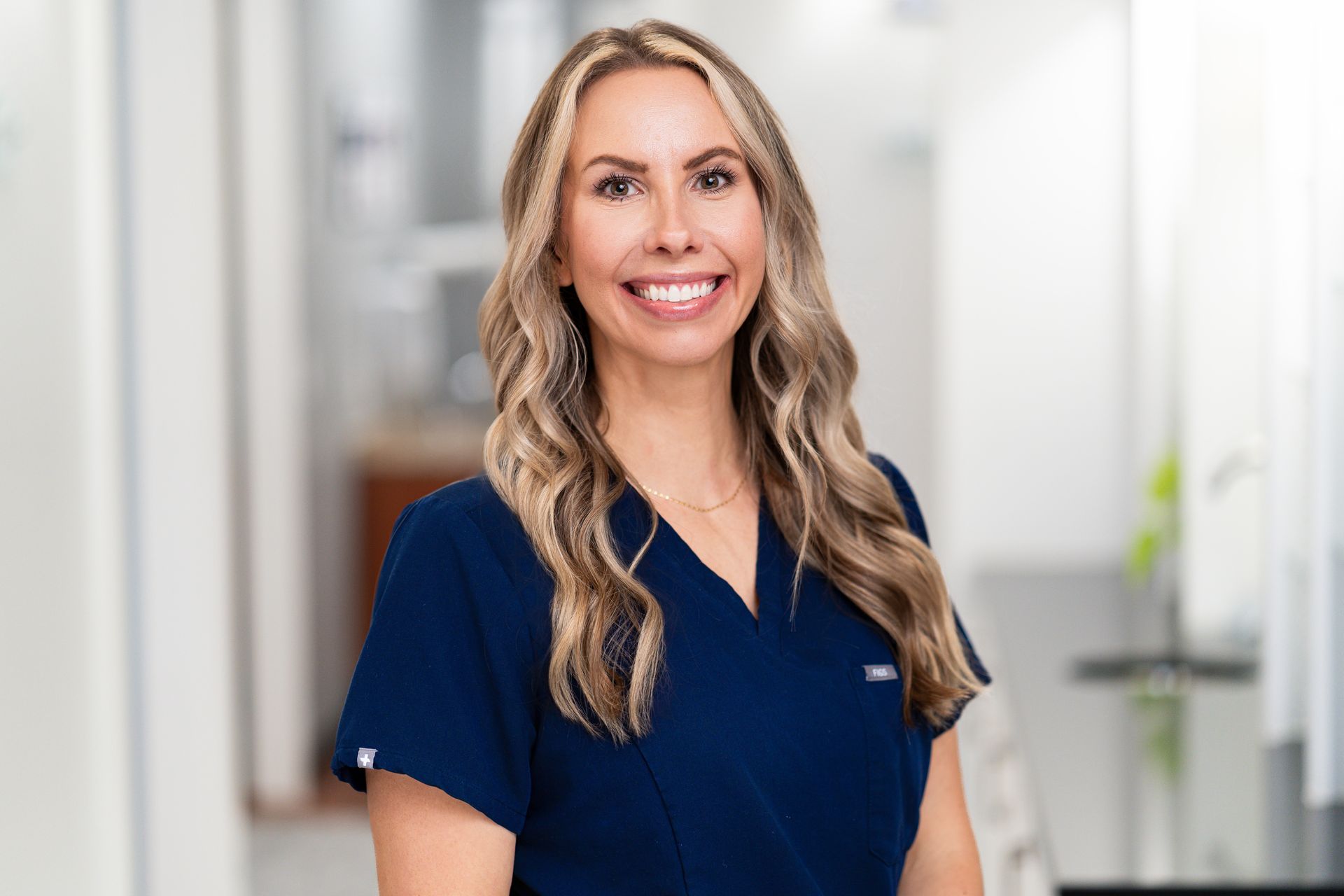 Woman with dark hair smiles, leaning on a white counter; tattoo on arm; black uniform; Hills sign in background.