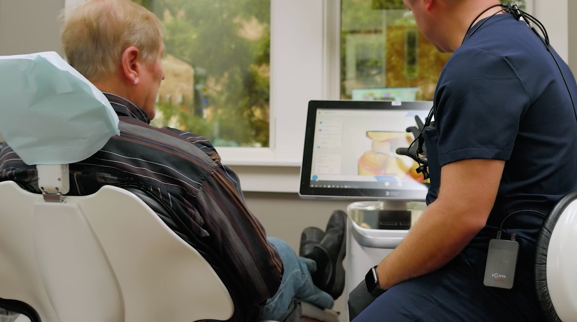 Person holding dental implants, dentist pointing to tooth. X-ray on laptop in the background.