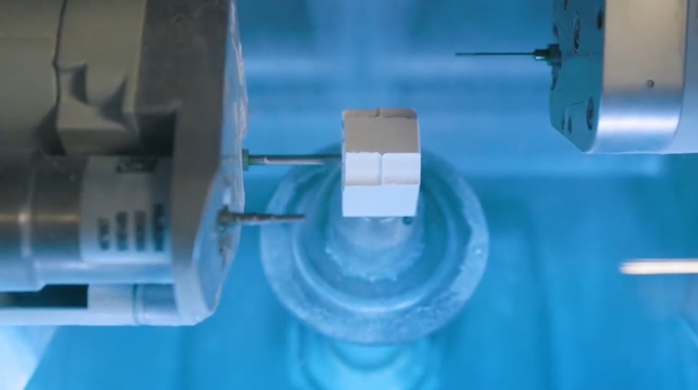 Hand placing a dental crown into a CEREC MC XL milling machine. Gray and white machine with blue light.