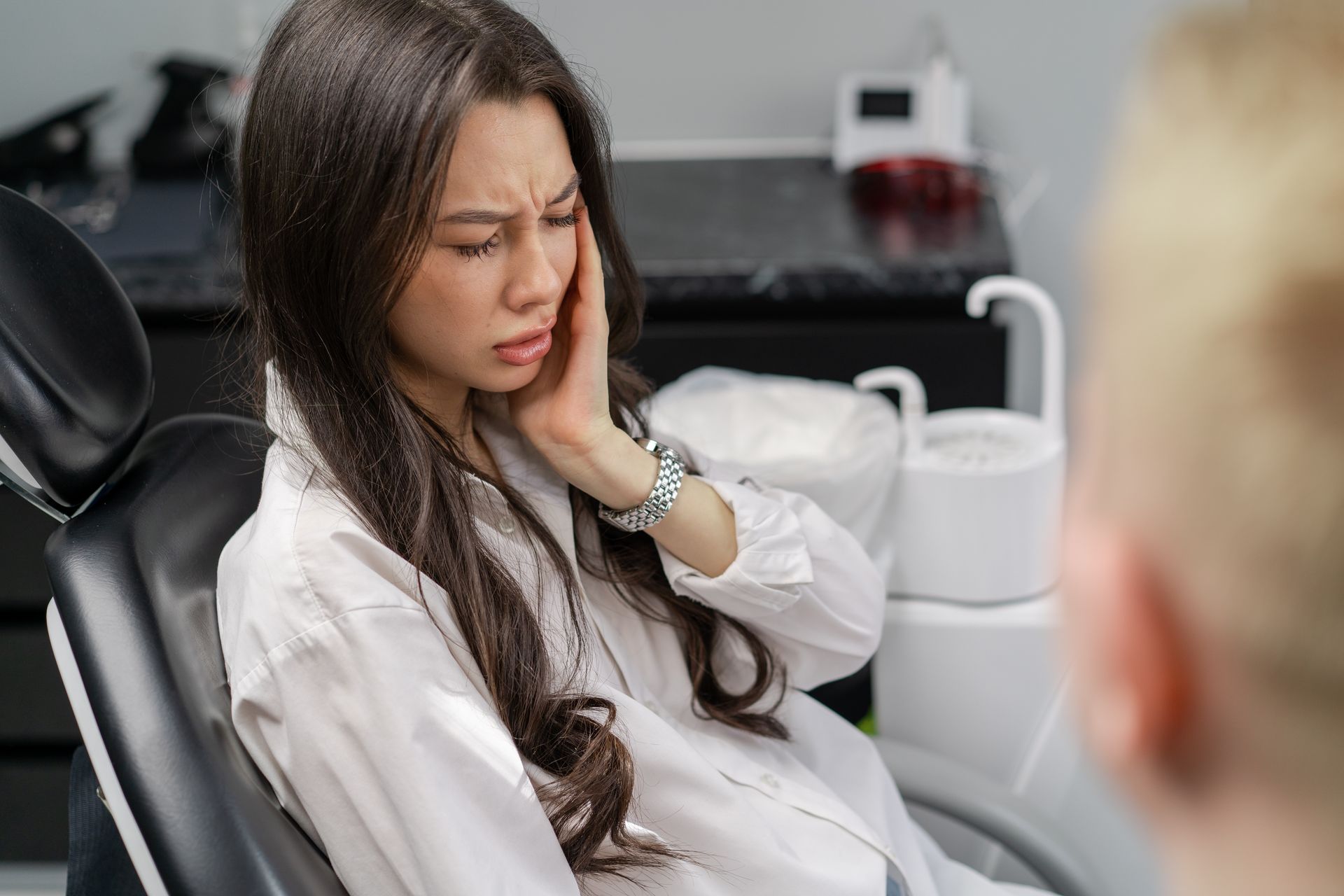 Dentist and assistant treating a patient in a dental office. Both wear masks, patient reclined.