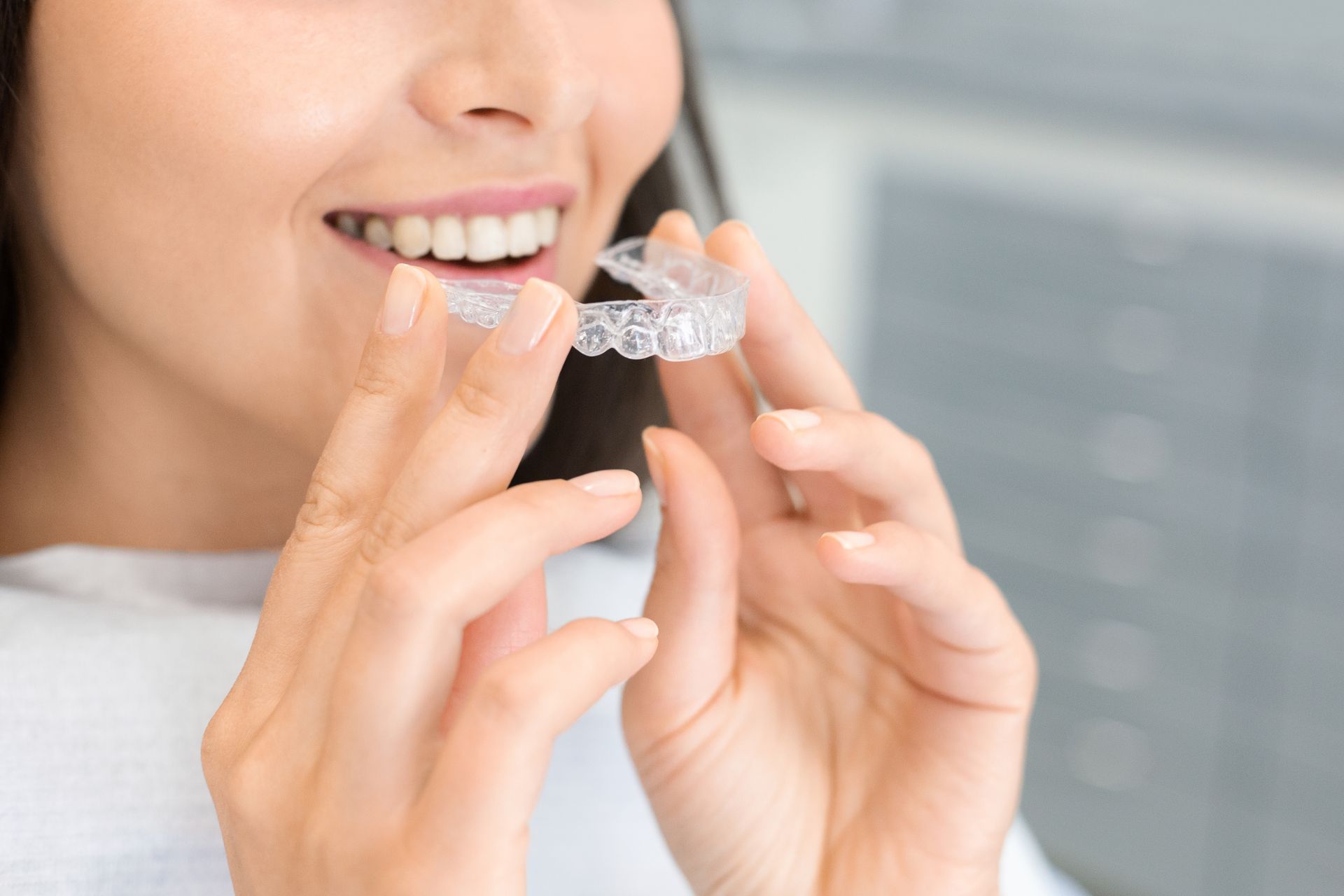 Hands holding two clear Invisalign aligners, against a blurred background.