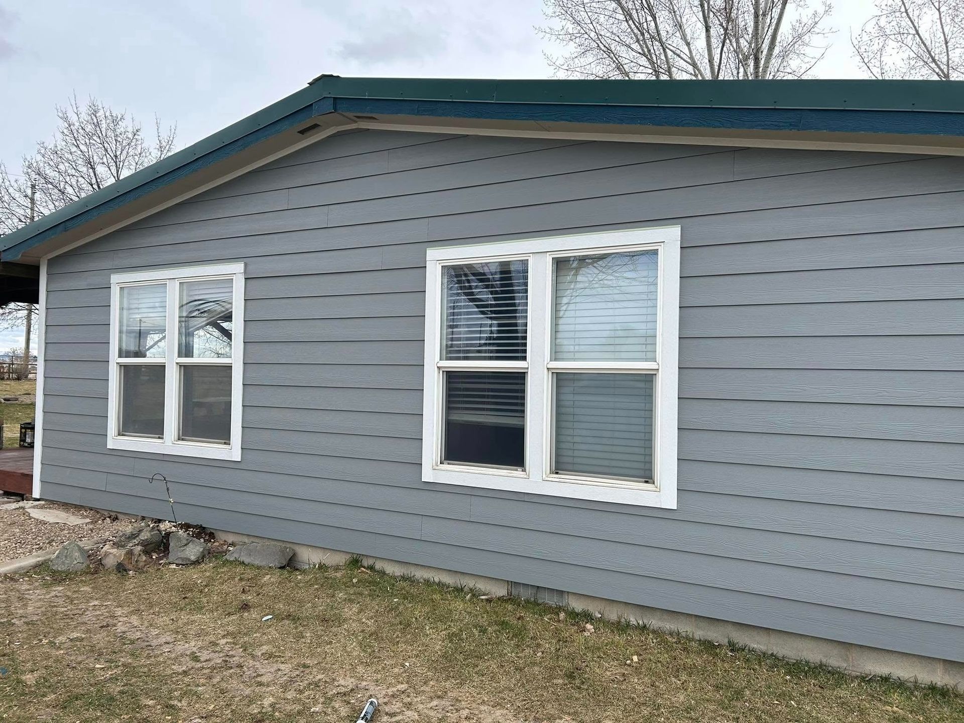 A gray mobile home with white windows and a green roof.